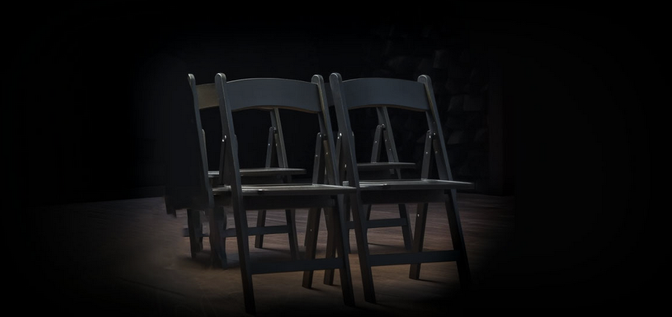 Four, empty black fold-up chairs on darkened stage